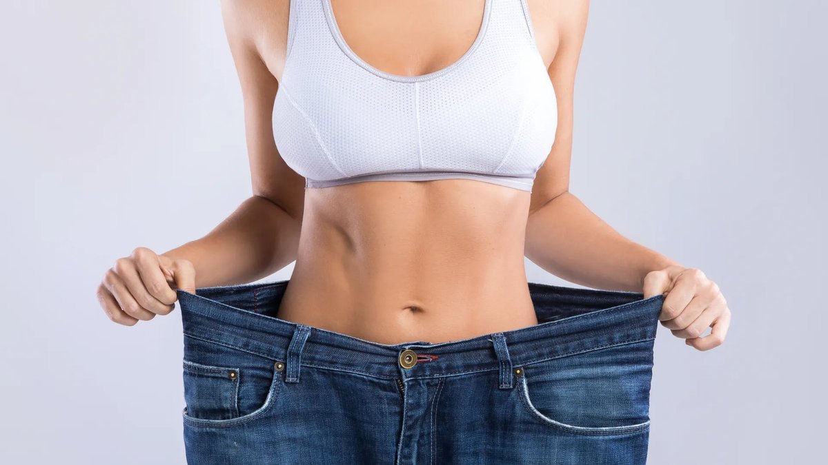 Mulher mostrando o quanto emagreceu ao segurar uma calça jeans larga, representando o emagrecimento estratégico