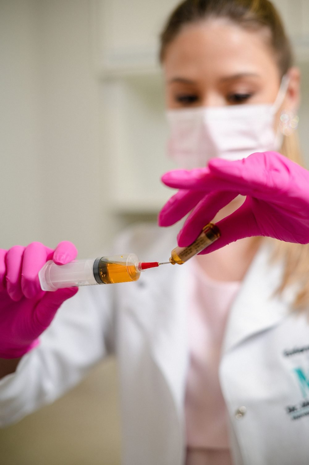 Profissional de saúde de luvas rosa preparando uma seringa, representando a reposição hormonal com acompanhamento médico